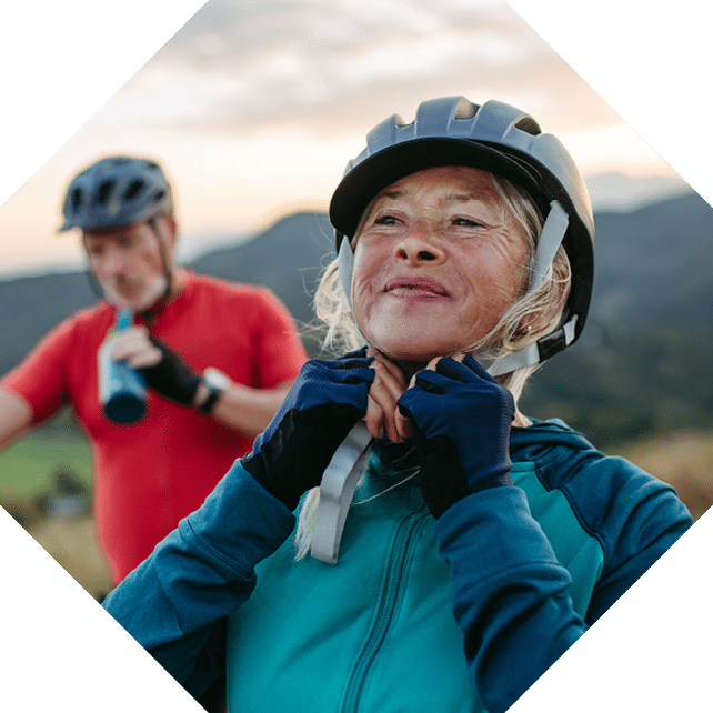 Portrait of beautiful senior couple on bike ride in autumn nature. Taking break, drinking water from sport bottle and fastening helmet.